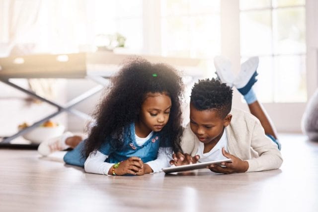 african-american boy and girl lying on the floor while looking at a tablet device